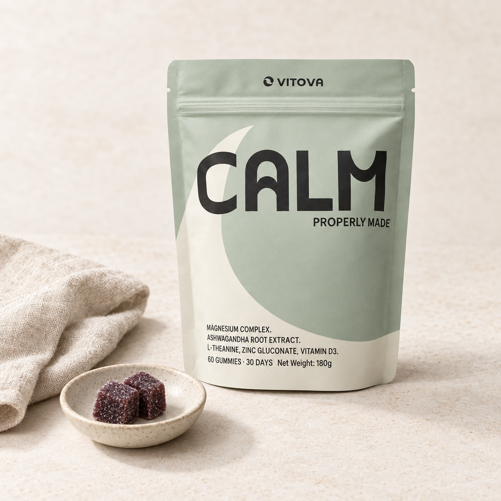 Sage-green Vitova Calm pouch beside a ceramic dish containing two dark burgundy gummies on a light stone surface.