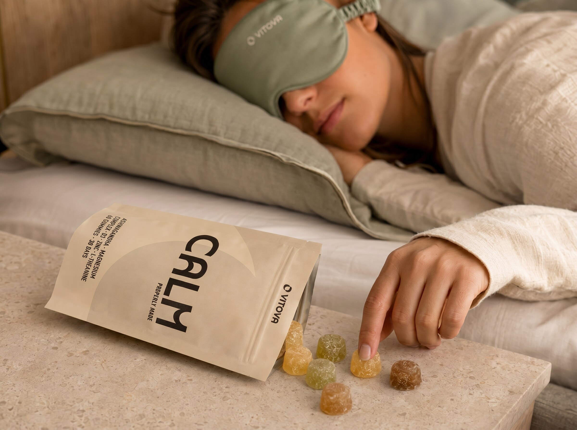 Vitova Calm pouch tipped open with gummies, beside a person resting on a pillow with a Vitova sleep mask